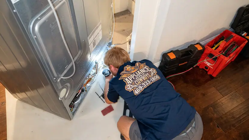 Top-down view of a technician working behind a refrigerator with tool cases beside him